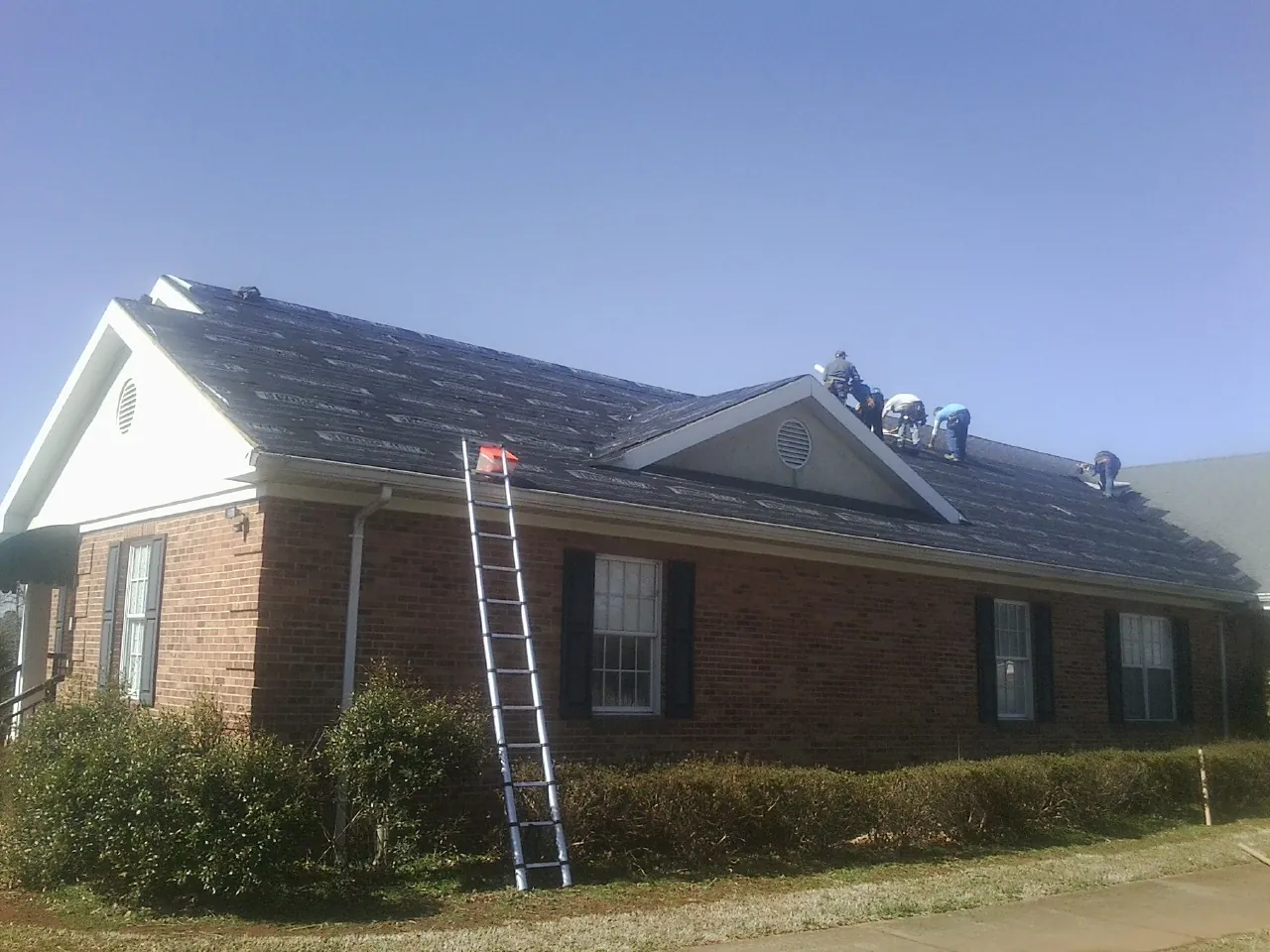 Crew tearing shingles off a brick ranch roof with a ladder set — Emergency Roof Repair work by our crew in Hawarden