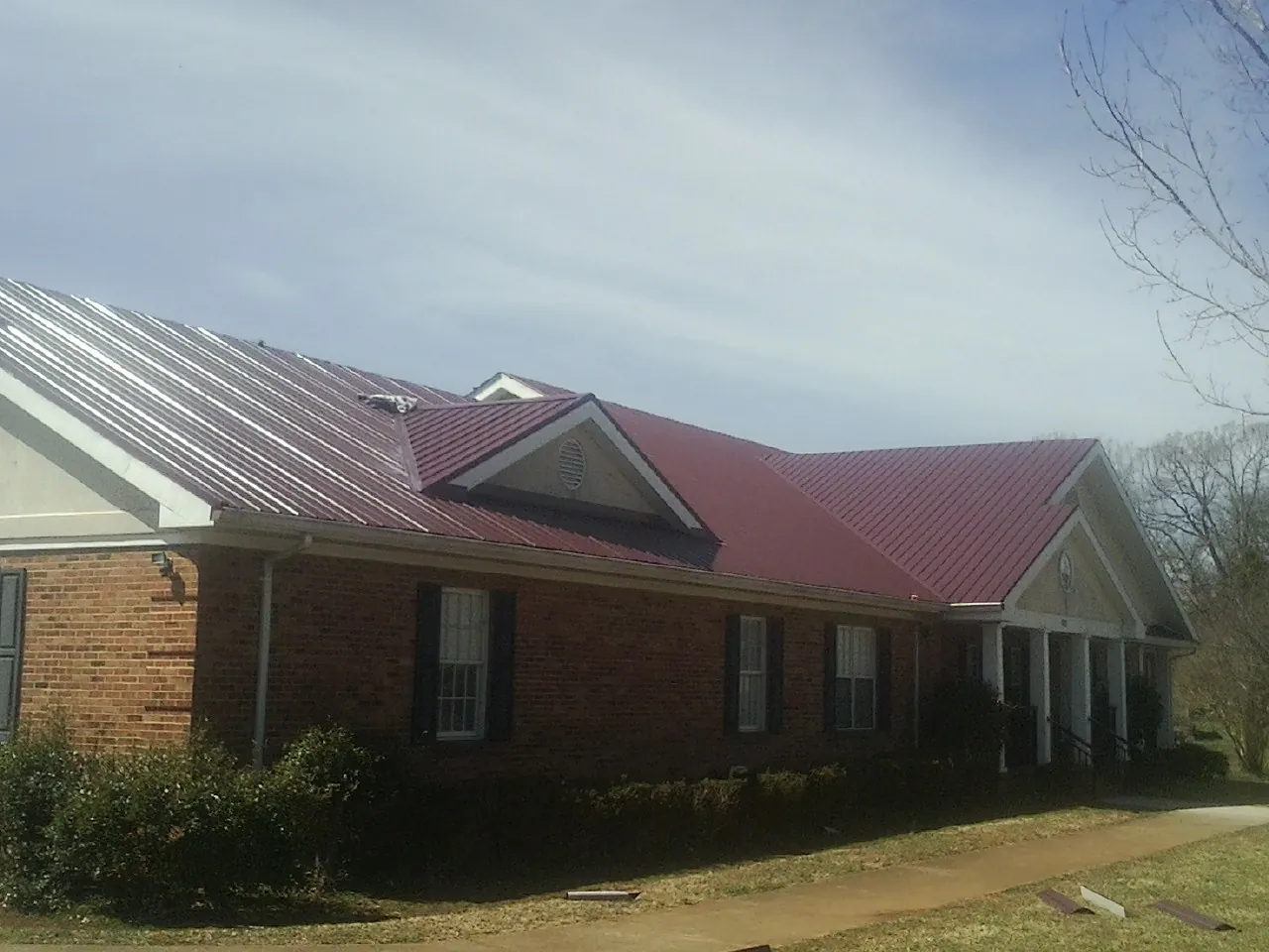 Red metal roof with gabled entries on a long brick building, from a Hail Damage Roof Repair job in Hawarden
