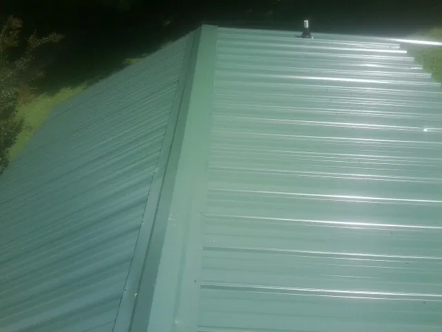 New green metal panels meeting at the ridge of a roof — Flat Roof Repair work by our crew in Hawarden