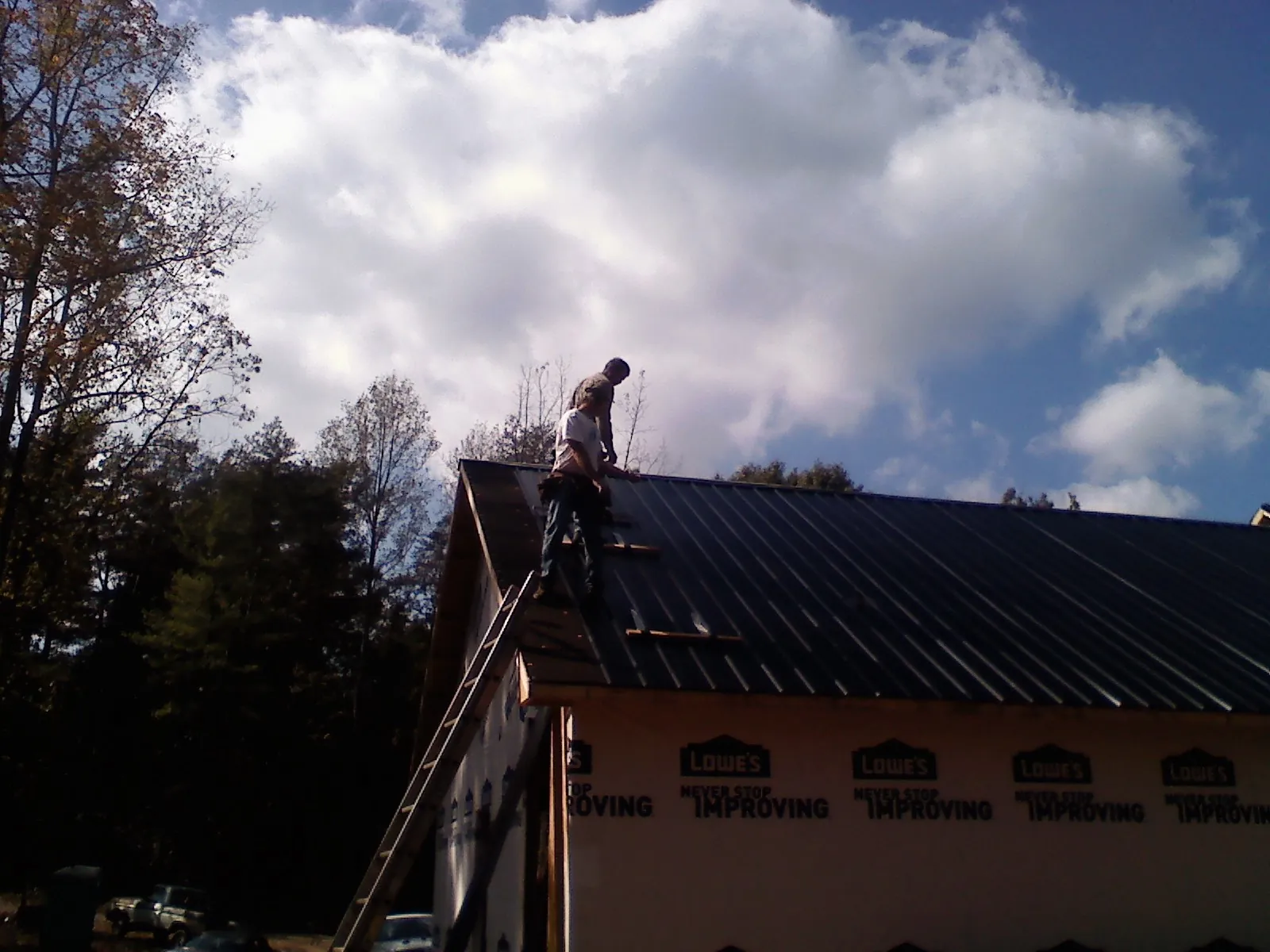 Roofer fastening dark metal panels high against a cloudy sky, from a Roof Inspection job in Hawarden