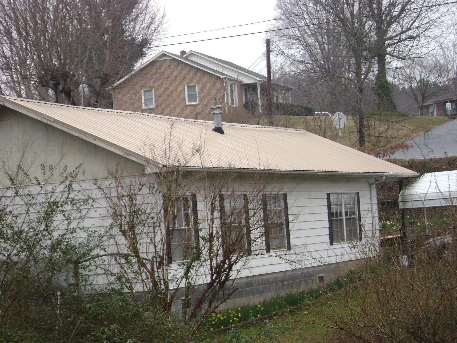 Tan metal roof on a white sided house set into a hillside — Commercial Roofing by Roofing Brothers in Hawarden