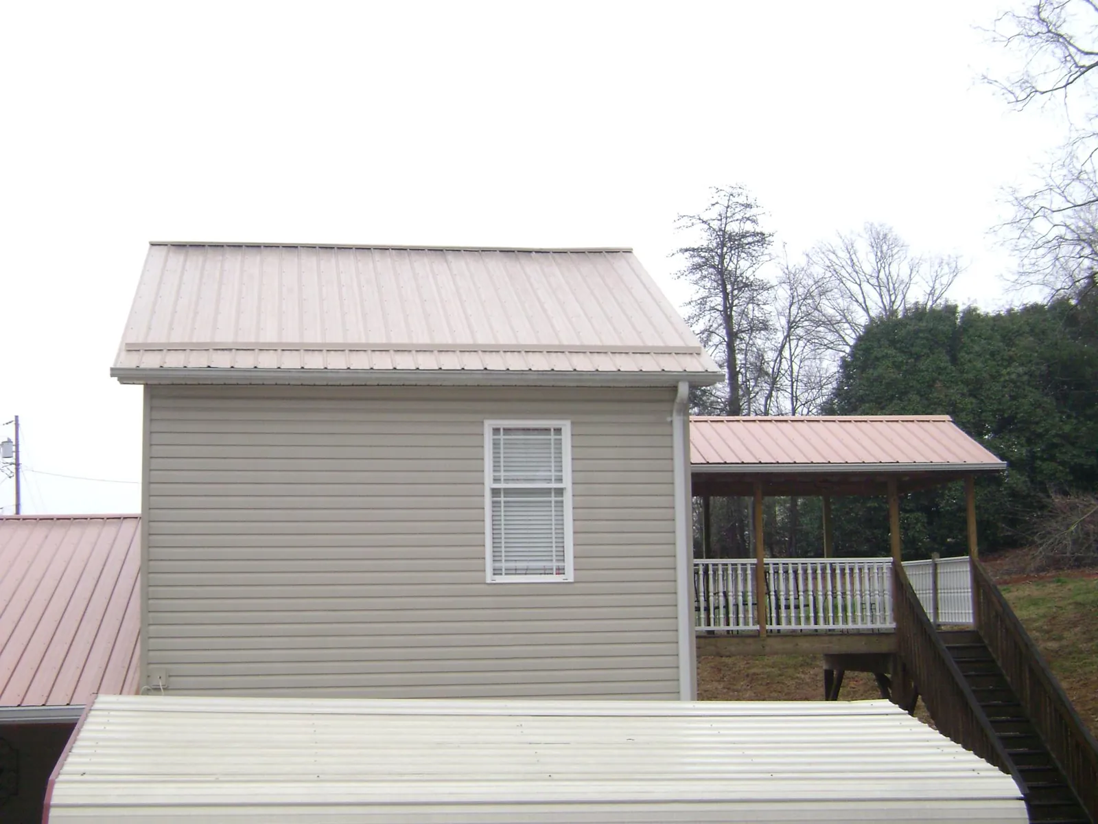 Tan metal roofs on a two story addition and attached porch, from a Roof Replacement job in Hawarden